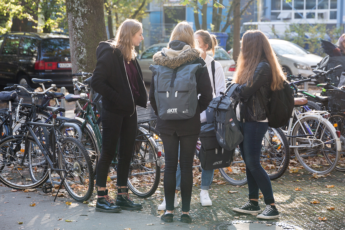 eine Gruppe Studentinnen auf dem Campus, eine davon mit KIT-Rcuksack,. Fahrräder im Hintergrund